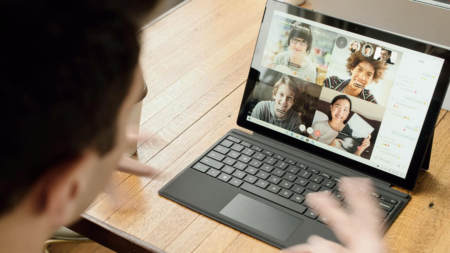 一个人正在与其他几个人进行视频会议，这些人的照片显示在一台笔记本电脑的屏幕上
