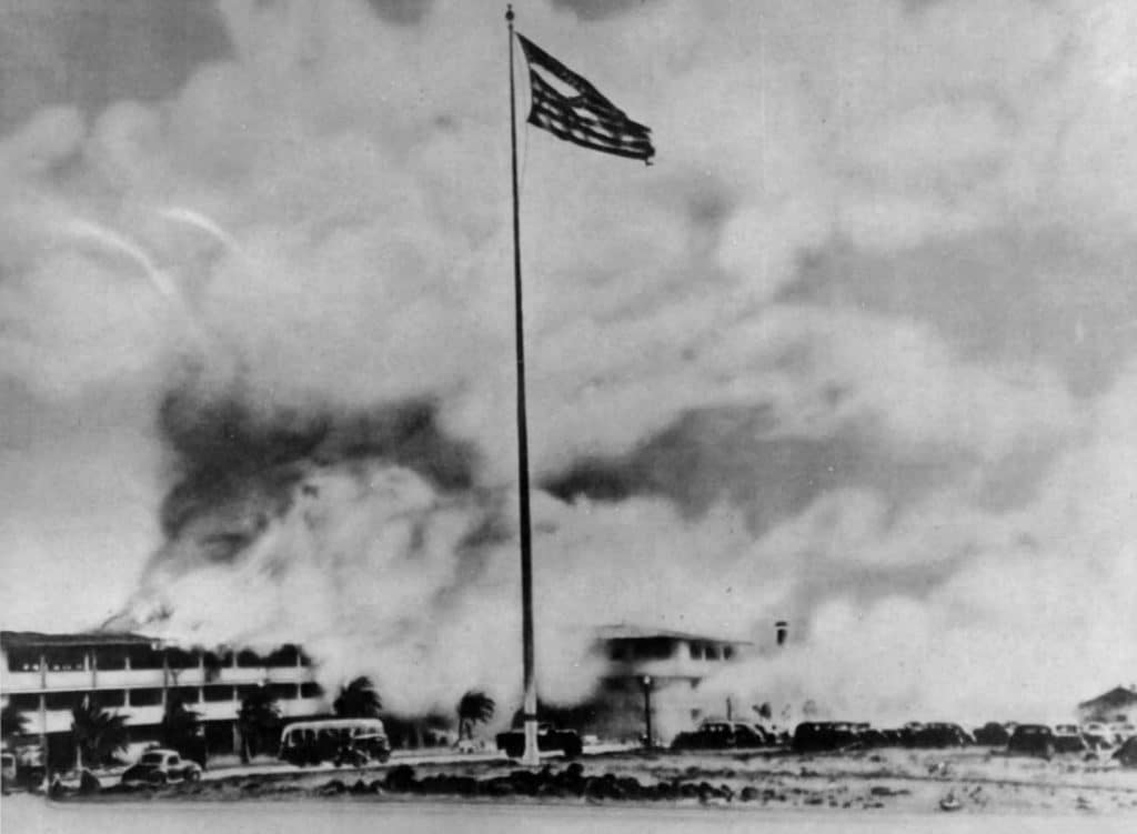 日本偷袭珍珠港后，希卡姆机场燃烧的兵营和旗杆上被撕碎的美国国旗。图片来源:国家公园管理局。