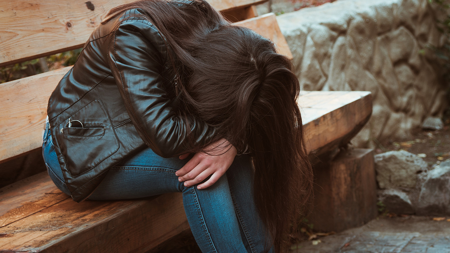 Young woman sitting on bench with head on arms, looking sad or depressed.