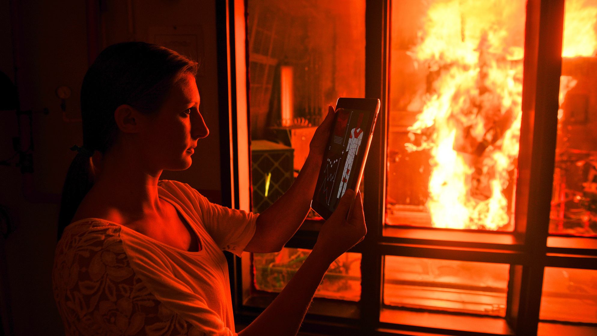 一个研究人员在iPad上查看结果，而PyroMan人体模型在一个玻璃房间里燃烧着
