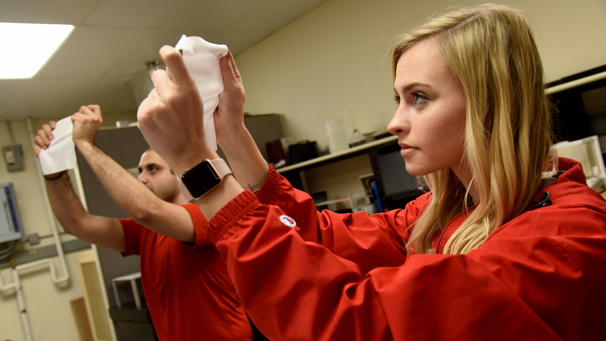 两个人在光线下举起白色织物的样本，同时拉伸它们