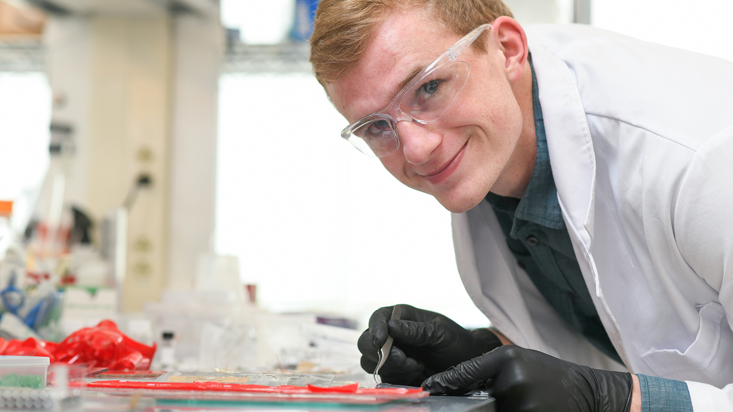 尼尔·鲍(Neil Baugh)俯身在实验室的长凳上，对着镜头微笑。