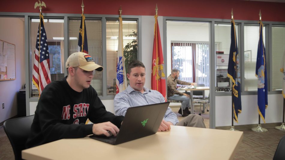 一名学生和工作人员在军事和退伍军人服务办公室的一张桌子上谈论