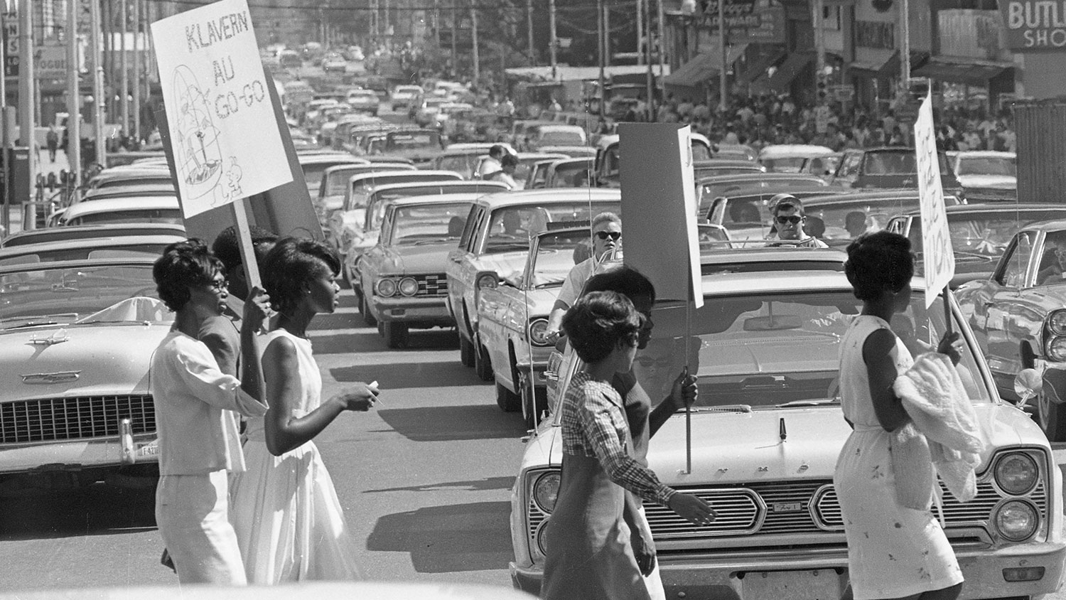 一名抗议者穿过街道，在这张六十年代的黑白照片中，他举着一个牌子。