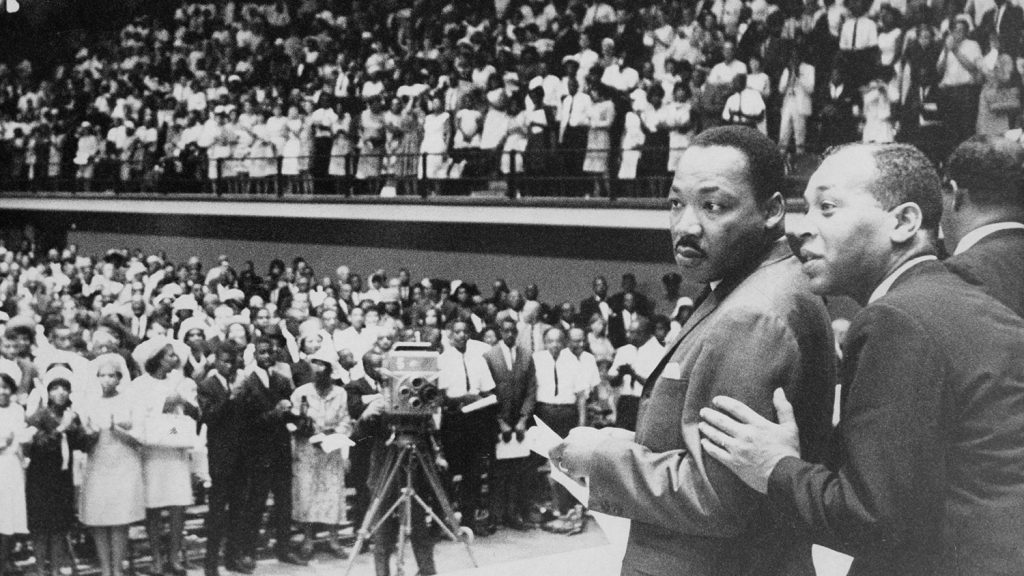 Martin Luther King Jr.于1966年7月31日，在雷诺大学举行的综合人群中，准备在Reynolds Coliseum举行舞台，以上有5,000人和一个Unc-Teamience。[照片由北卡罗来纳州的国家档案提供。]