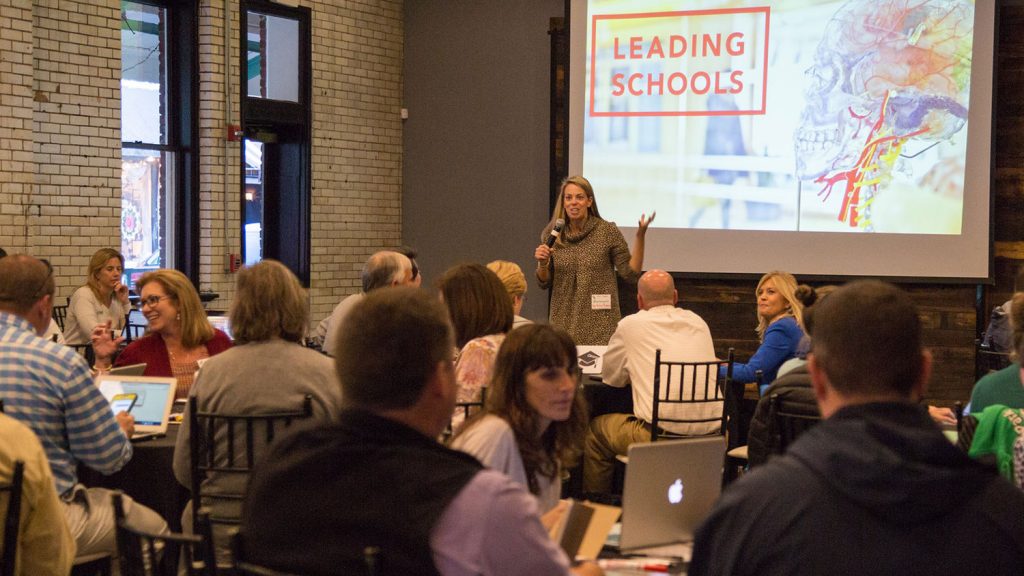 一名女子在一屋子人面前拿着麦克风讲话