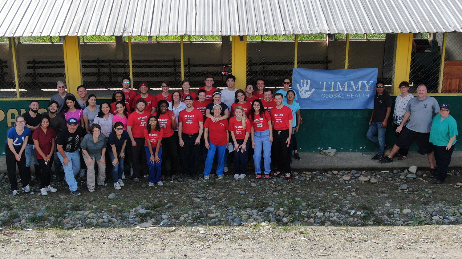 一群学生和领导人穿着NC州衬衫站在厄瓜多尔一家乡村诊所外，上面挂着TImmy全球健康的横幅