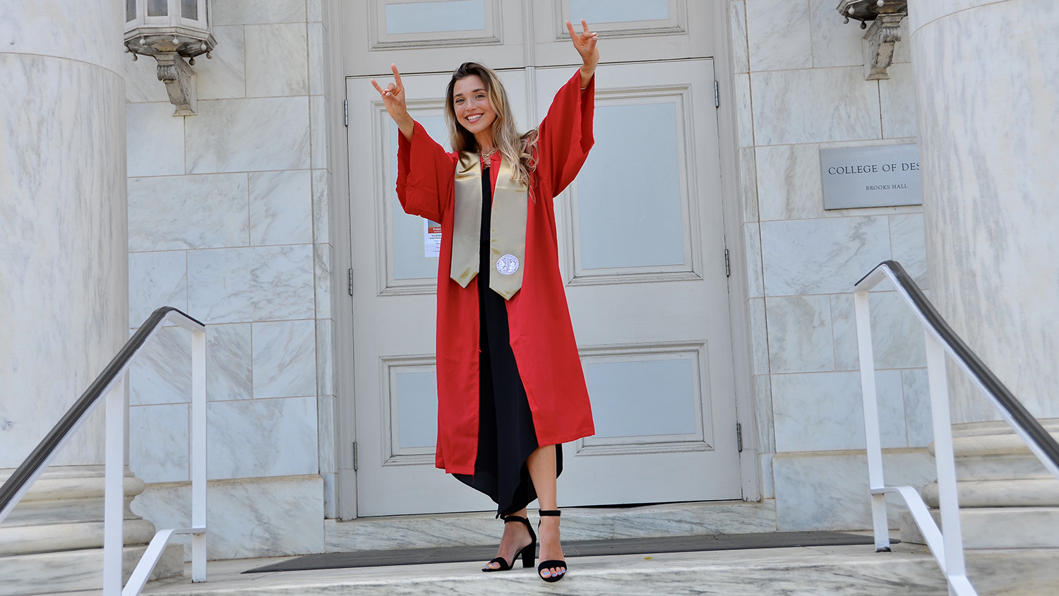 在设计大厦学院的石头前台，Katherine Hord姿势与狼手在她的红色毕业长袍。