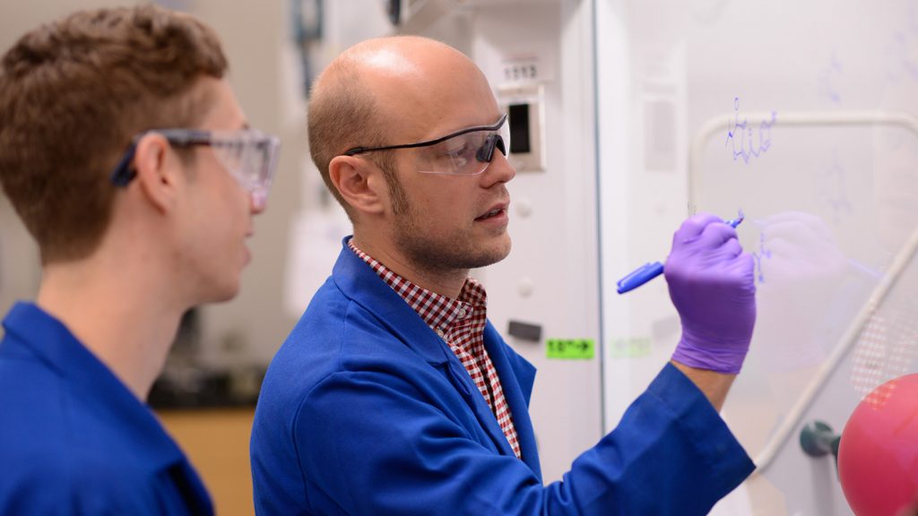 Josh Pierce和一名研究生素描分子模型在他的实验室中的白板上