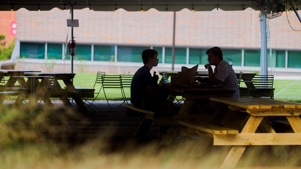 学生在百年校园的椭圆形的帐篷下的一个野餐桌子一起吃午餐。