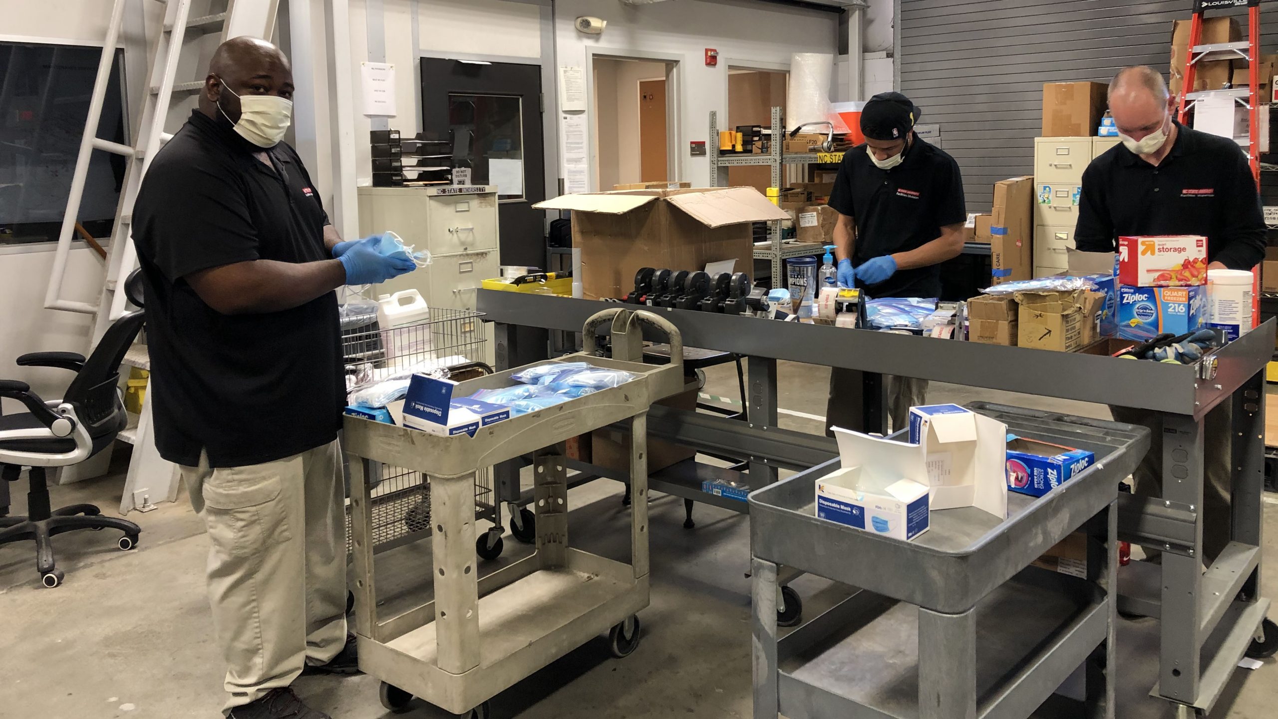 在校园仓库中，三家设施员工为工人的欢迎套件准备材料。