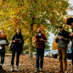 在一个色彩缤纷的秋日，一群学生和一位教授站在外面围成一圈。