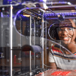 一位年轻女子站在一台3D打印机后面。