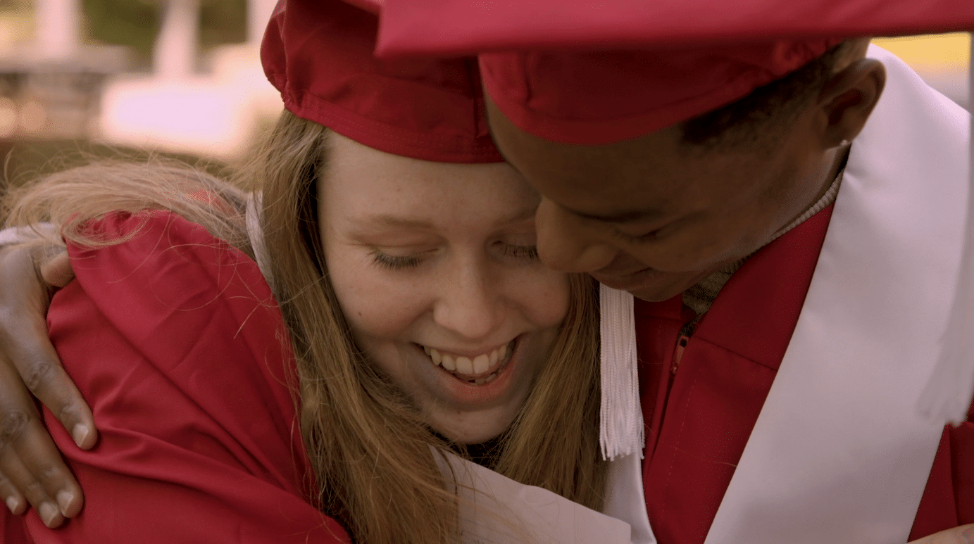 Sara Altman and Justin Mason share a hug while wearing their graduation caps and gowns.