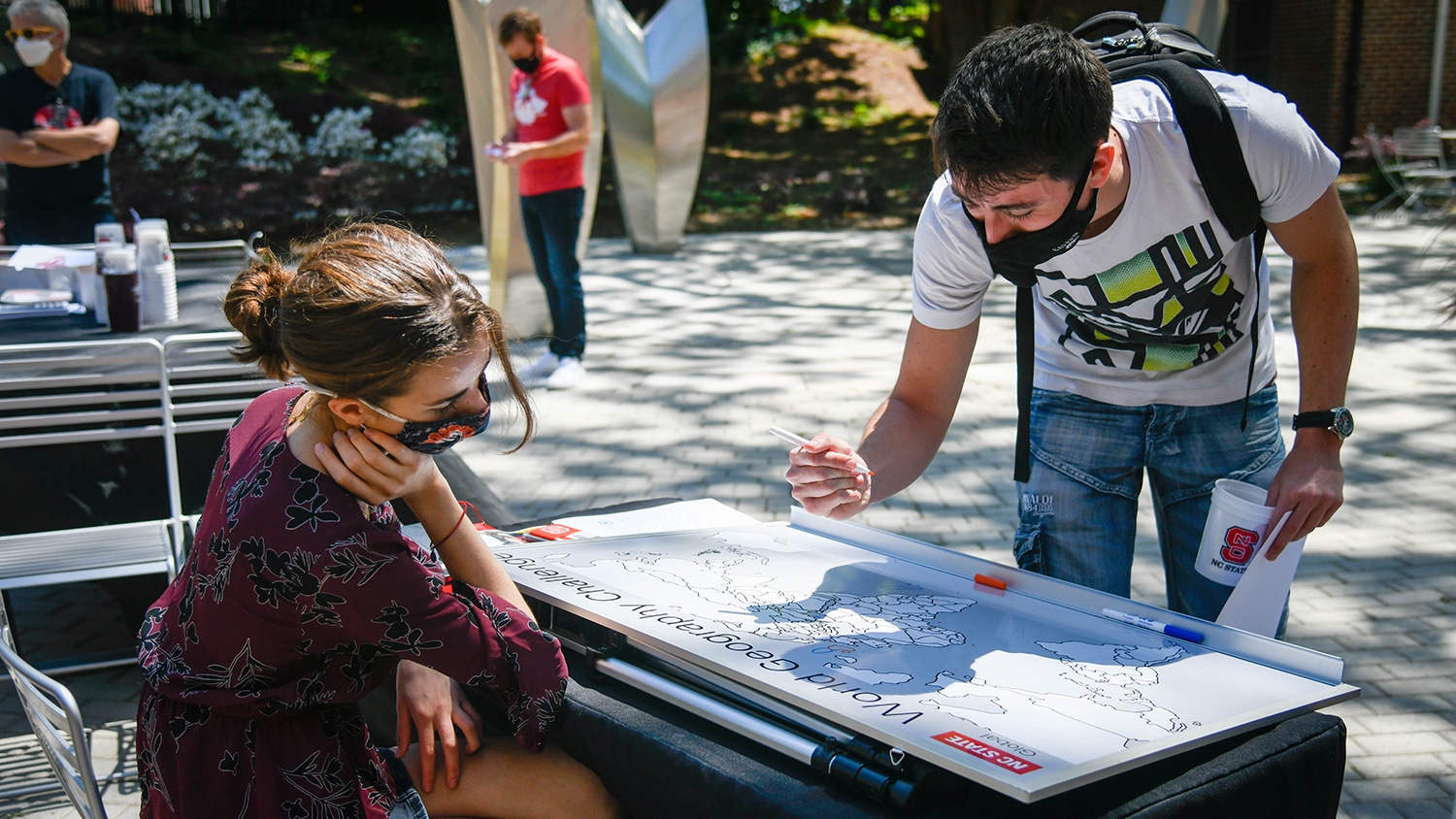 一个男学生在世界地图上标出他的家乡，而一个女学生在看着。
