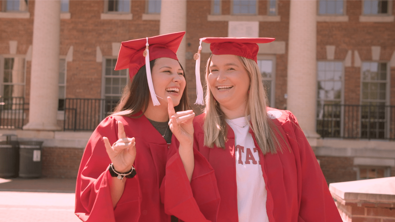 艾米丽·贝尔贝尔和玛丽·凯瑟琳·金利戴着毕业帽和学士服，竖起狼耳朵在北卡罗来纳州法院摆姿势。