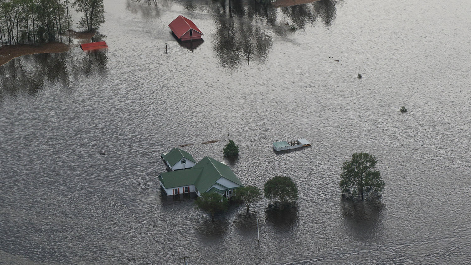 从空中俯瞰洪水中的农舍、车辆和附属建筑。所有的结构都被淹没了，只有屋顶暴露在外