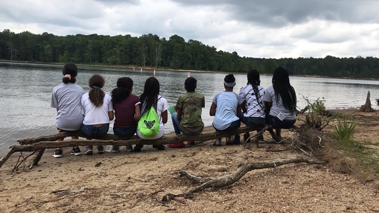 一群中学生坐在一根圆木上，眺望着一个湖。