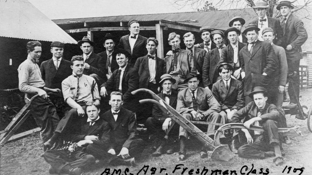 一群男人拿着农具摆姿势的黑白照片。照片底部写着“1909年新生班”。