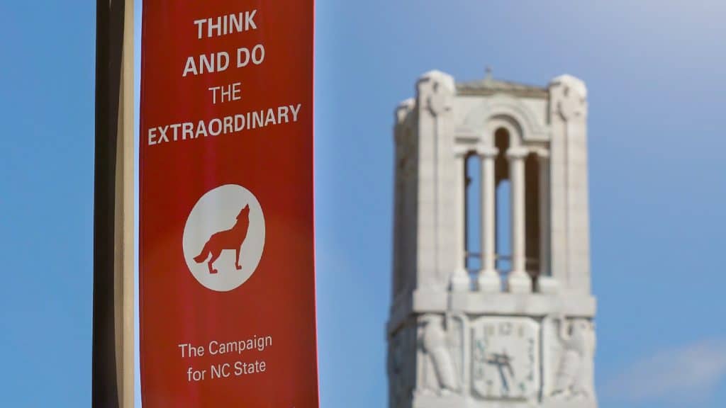 在纪念钟楼附近，悬挂着一条红色的横幅，上面有一只狼的标志，上面写着“思考，做非凡的事:为北卡罗来纳州而战”。