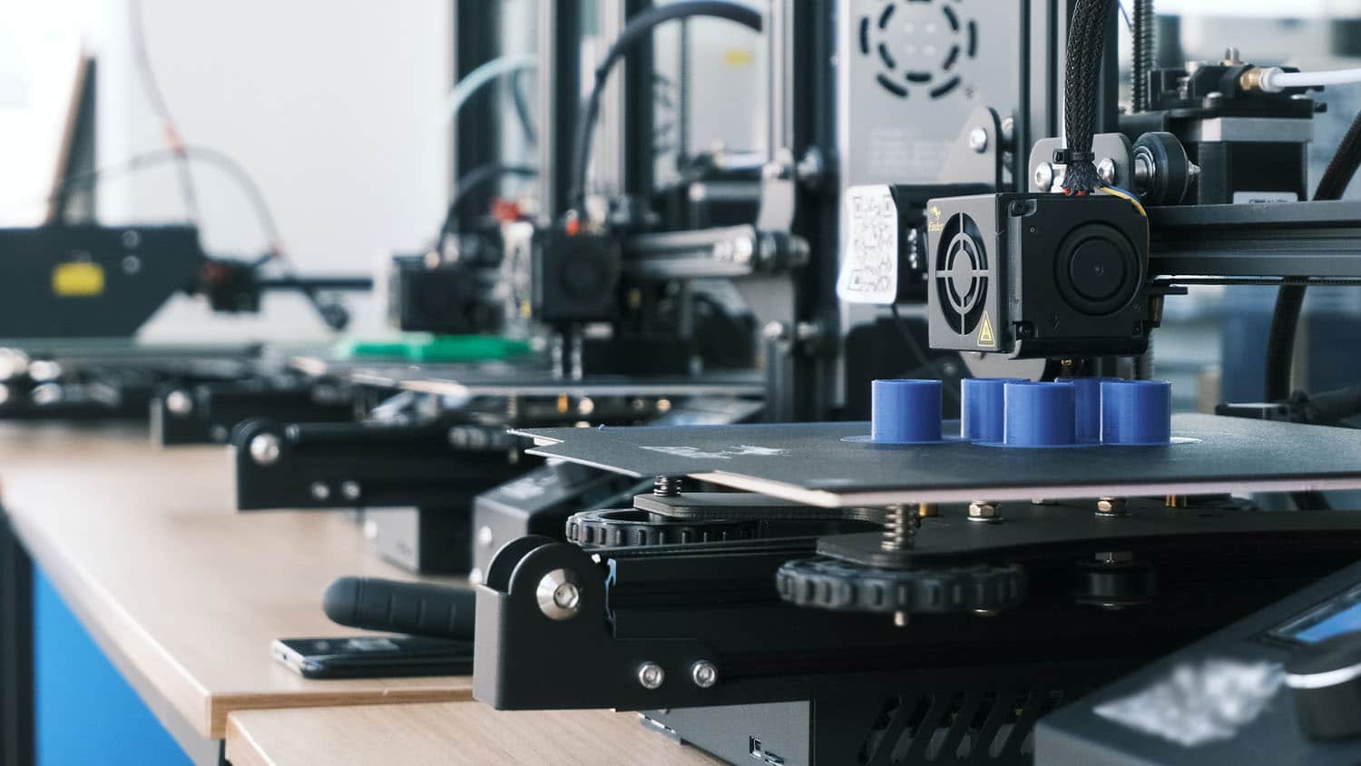 几台3d打印机排在工作台上;其中一个是打印一个物体
