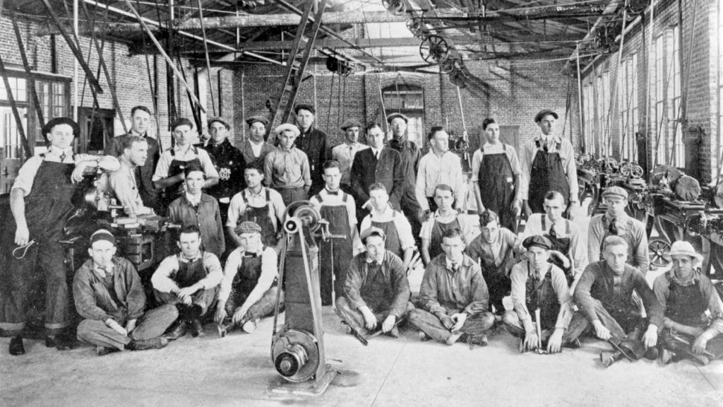 这是一张黑白照片，一群穿着工作服的男人在一间工程教室里摆姿势。