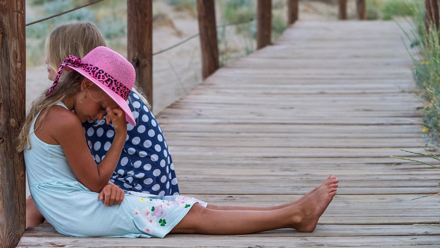 两个孩子坐在码头上;一个孩子面朝别处，另一个低着头