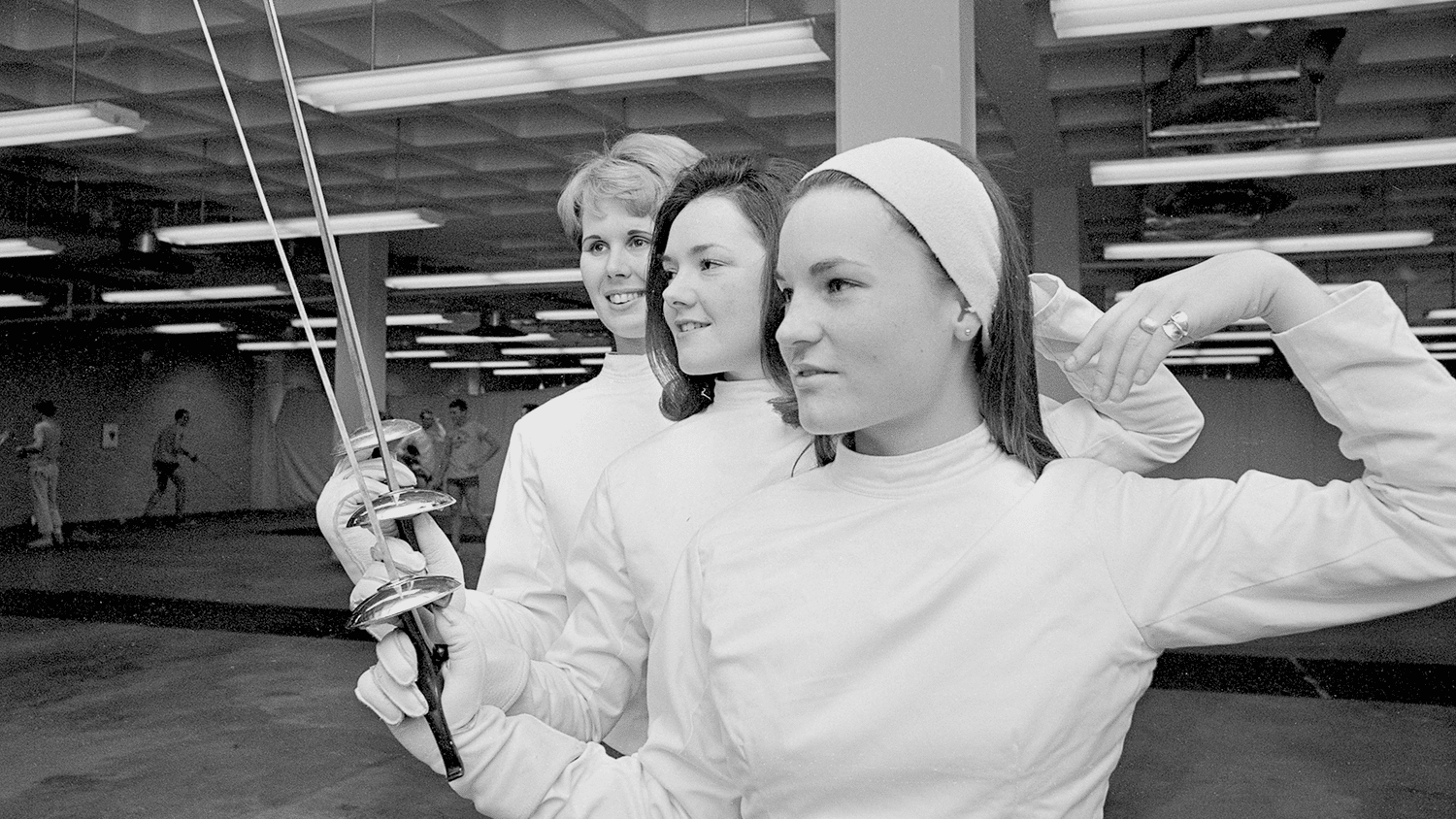 Three women hold foils in a ready position. The image is in black and white.