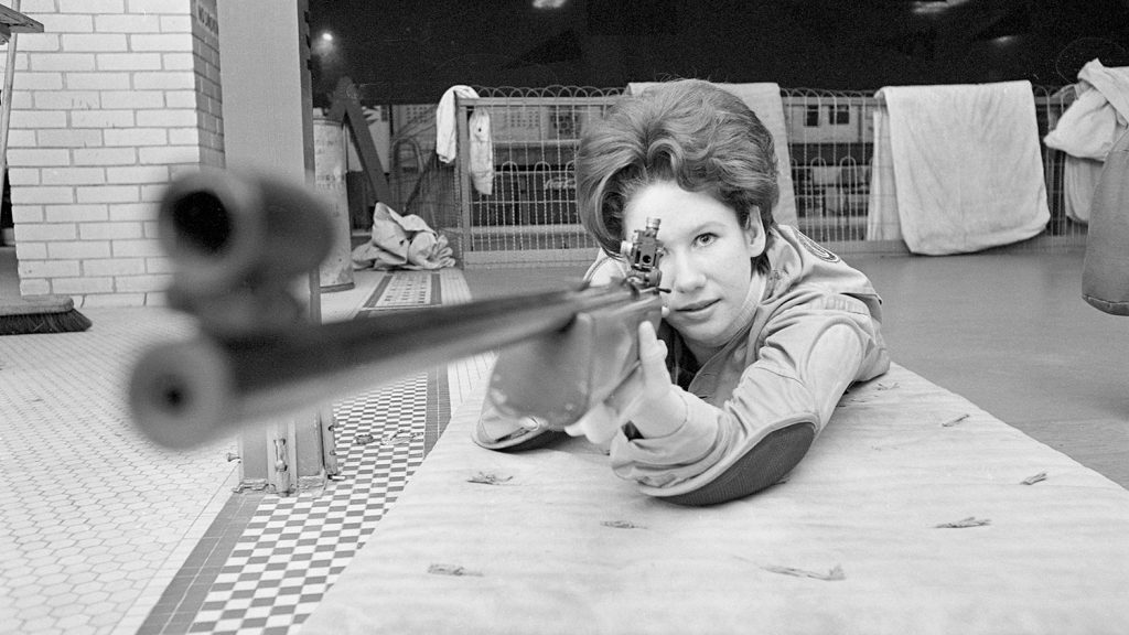 Alma Williams aims a rifle forward. This photo is in black and white.