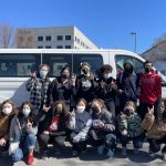 A group of students pose in front of a van outside of Habitat For Humanity.
