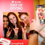 Students hold up wolf hands while posting in a cutout frame for Day of Giving.