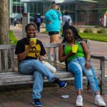 Two students drink lemonade together on a bench.