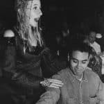 在一张黑白档案照片中，一名身穿中世纪长袍的学生在牧歌晚宴上唱歌，她的手搭在一位观众的肩膀上。