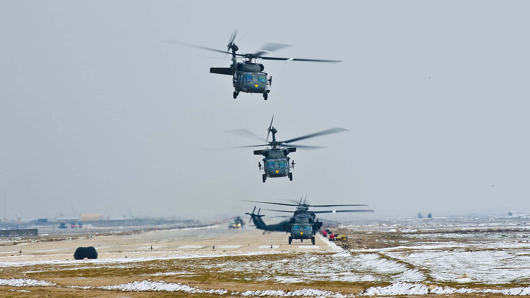 四架军用直升机在一个下雪的机场上紧挨着起飞