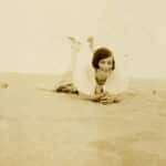 A sepia-toned photos shows a late adolescent Mary Yarbrough smiling at the camera as she lays on her stomach atop a sand dune at Kill Devils Hills in North Carolina's Outer Banks.