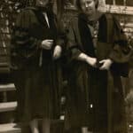 An adult Mary Yarbrough poses beside an unidentified woman on the steps leading to a building. Both women wear dark-colored doctoral robes.