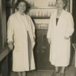 An adult Mary Yarbrough poses standing beside an unidentified woman in a laboratory stocked with scientific equipment. Both women wear white lab coats.