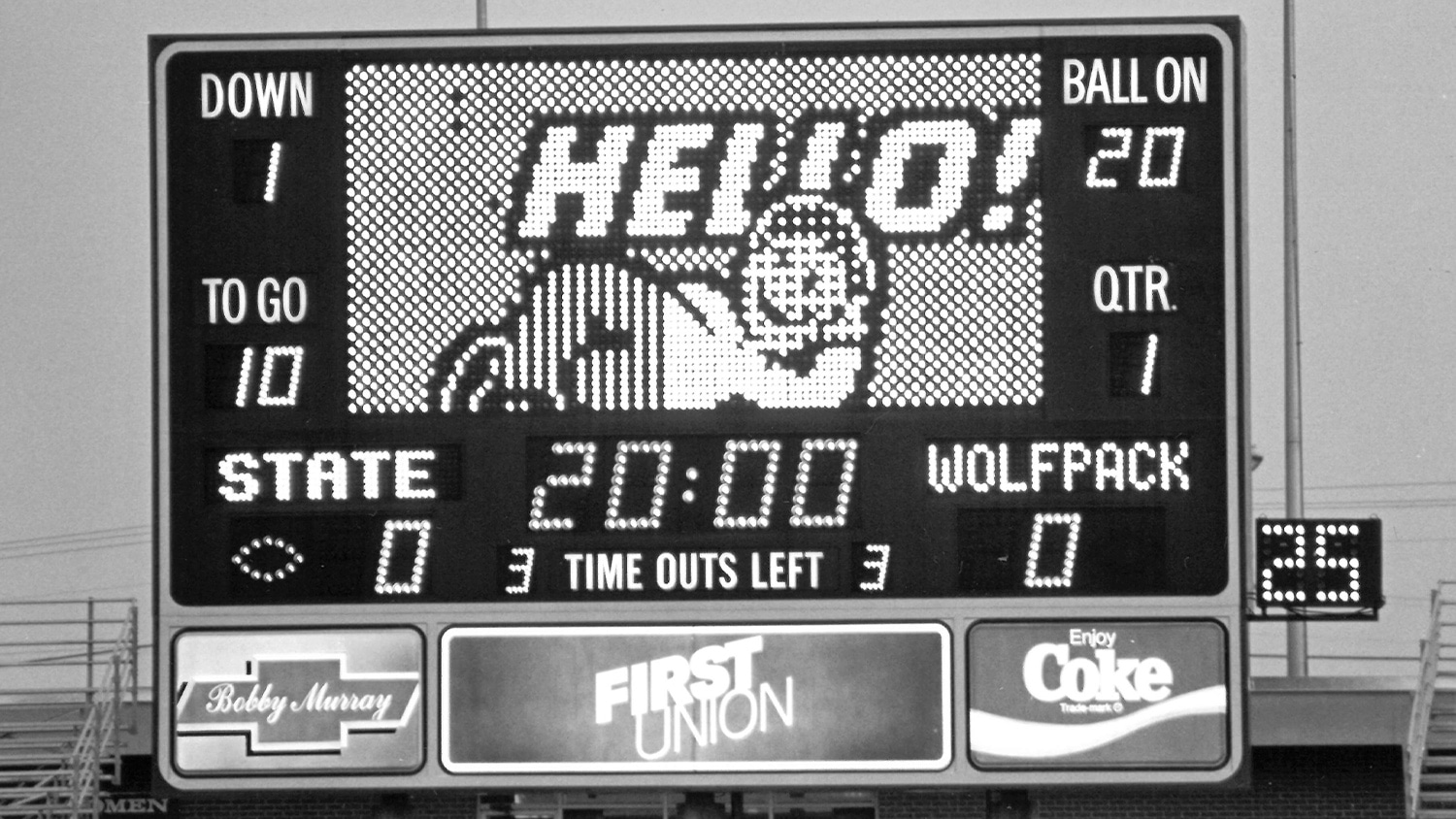 A black and white photo of the scoreboard in Carter-Finley Stadium in 1985 with a cartoon character saying Hello on the main screen