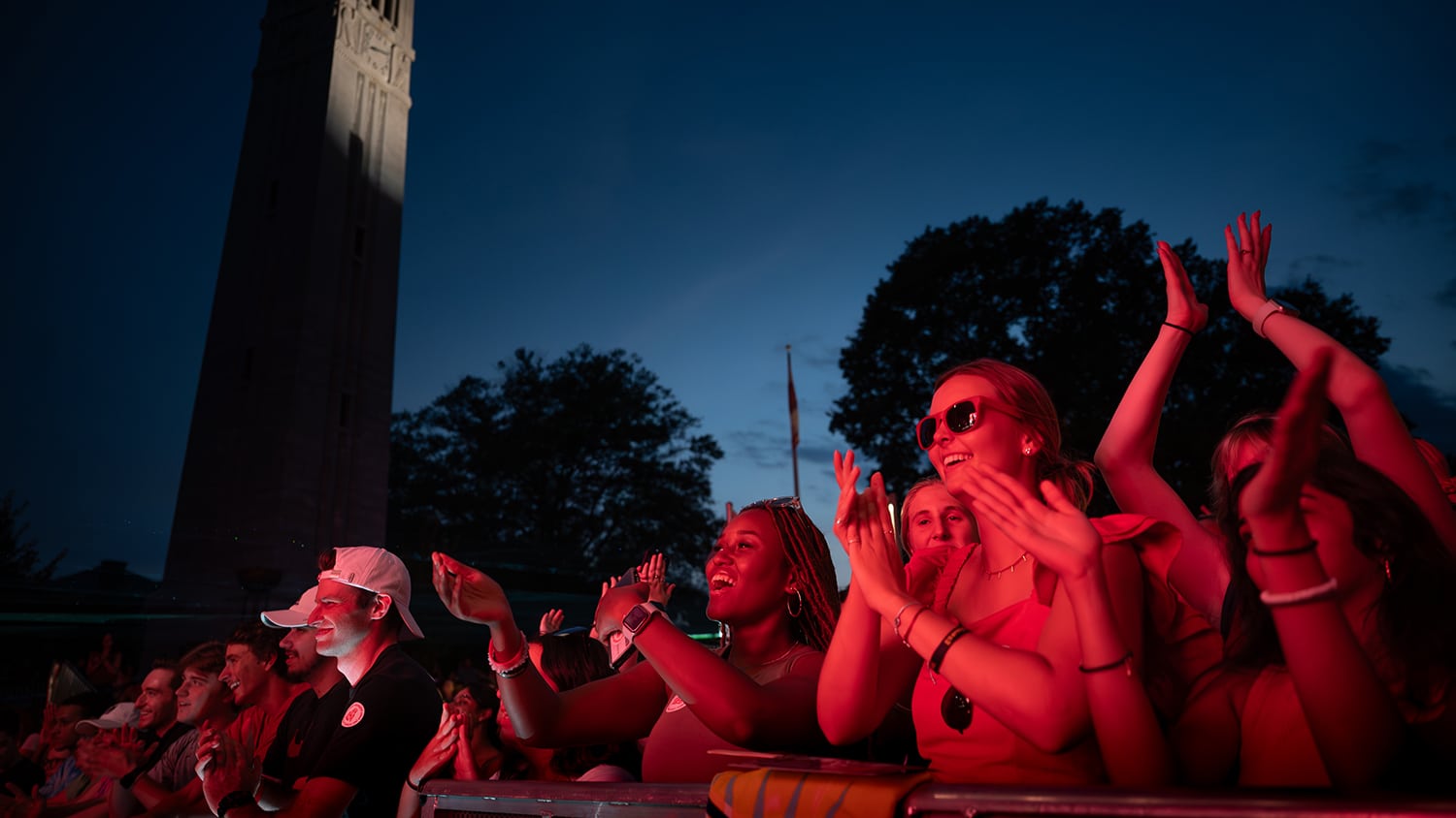 A group of students cheers during a concert at Packapalooza, with the belltower in the background.
