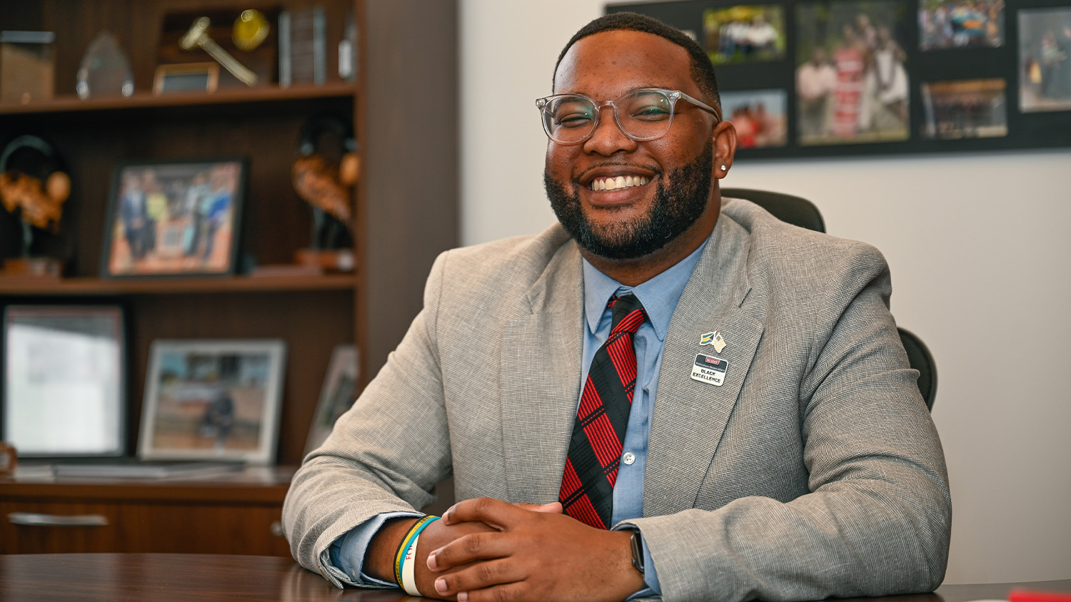 Jameco McKenzie sitting at the desk in his office, wearing a gray suit jacket with a red and black tie.
