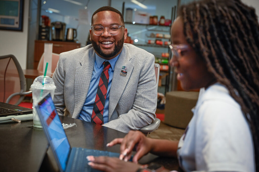 McKenzie sitting at a table and chatting with a student who is working on a laptop