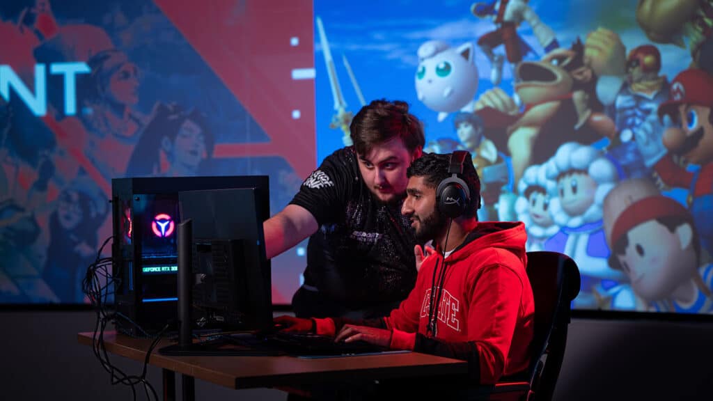 拍到两位学生在计算机机台协作,带多色视频游戏字符图片显示后台屏幕上